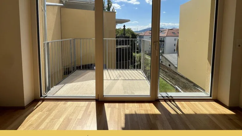 Helles Zimmer mit Holzboden und Zugang zu einem Balkon mit Stadt- und Bergblick.