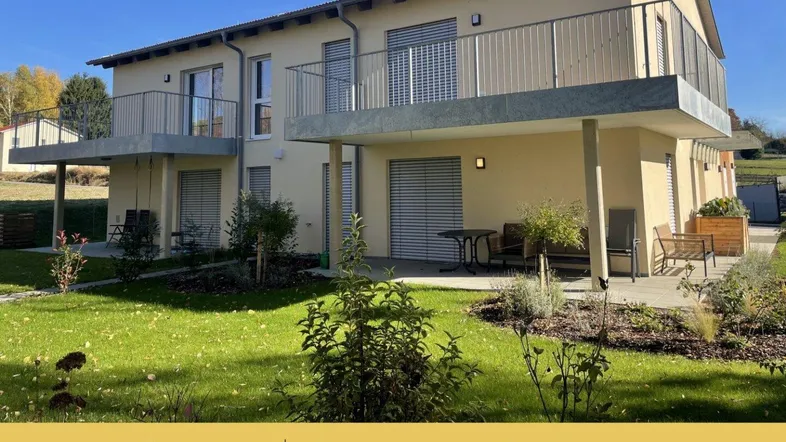 Moderne Doppelhaushälfte mit Balkonen, Terrasse und gepflegtem Gartenbereich unter blauem Himmel.