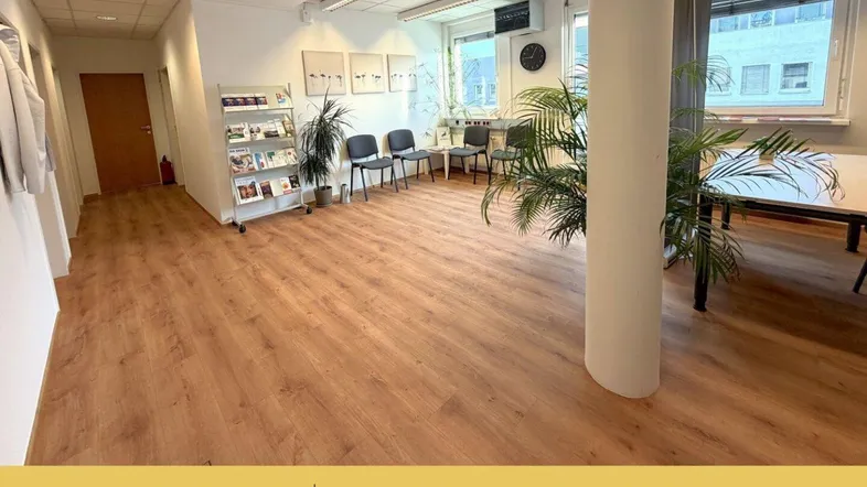 Geräumiges Büro mit hellem Laminatboden, großen Fenstern und Pflanzen, ideal für eine angenehme Arbeitsatmosphäre.