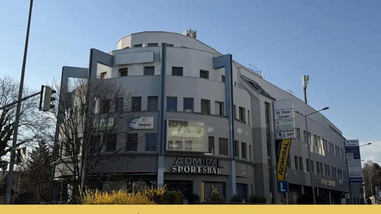 Ansicht des modernen Bürogebäudes mit Geschäften im Erdgeschoss und markanter Architektur unter blauem Himmel.