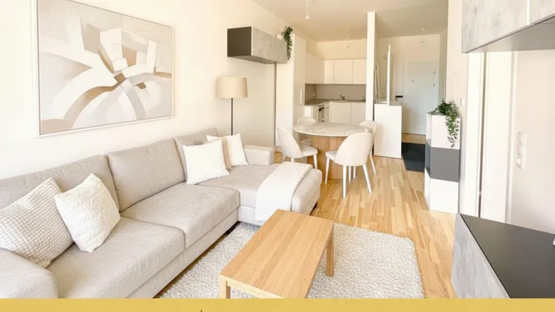 Helles Wohnzimmer mit offener Küchenzeile, Parkettboden und modernem Sofa.