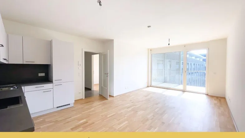 Heller offener Wohnbereich mit integrierter Küche, Parkettboden und Zugang zu einem Balkon.