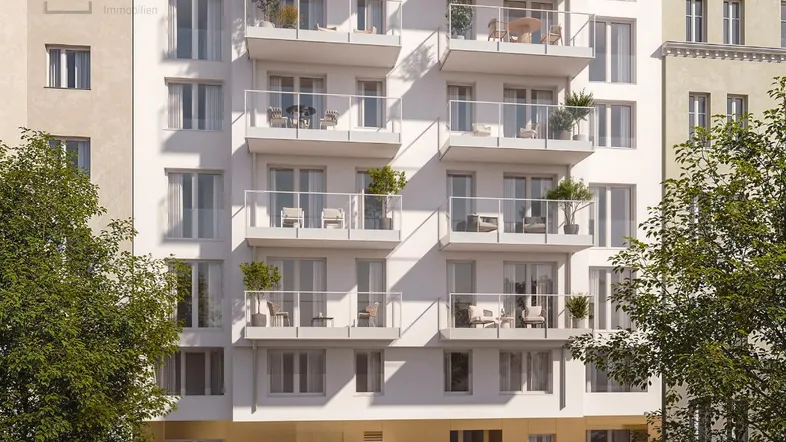 Moderne Wohnhausfassade mit vielen Balkonen und großen Fenstern, umgeben von Bäumen und Autos.