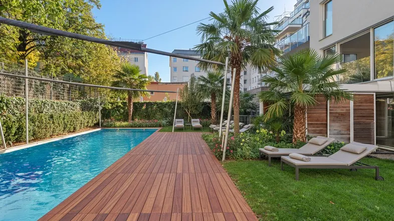 Außenbereich mit großem Swimmingpool, Holzterrasse, Palmen und Liegestühlen für Entspannung.