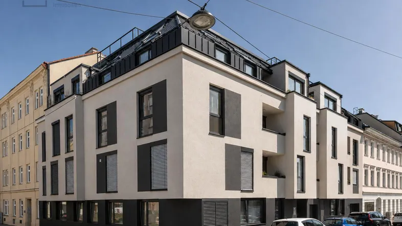 Modernes Eckgebäude mit heller Fassade und dunklen Akzenten in einer städtischen Umgebung.