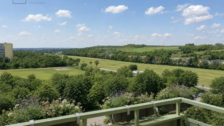 Blick vom Balkon auf weite grüne Felder und bewaldete Hügel unter blauem Himmel.