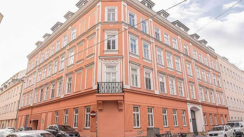 Historisches Eckgebäude mit orangeroter Fassade und kleinem französischen Balkon in städtischer Umgebung.