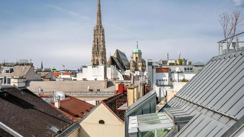 Panoramablick über die Dächer der Stadt mit historischer Kirche und moderner Dacharchitektur.