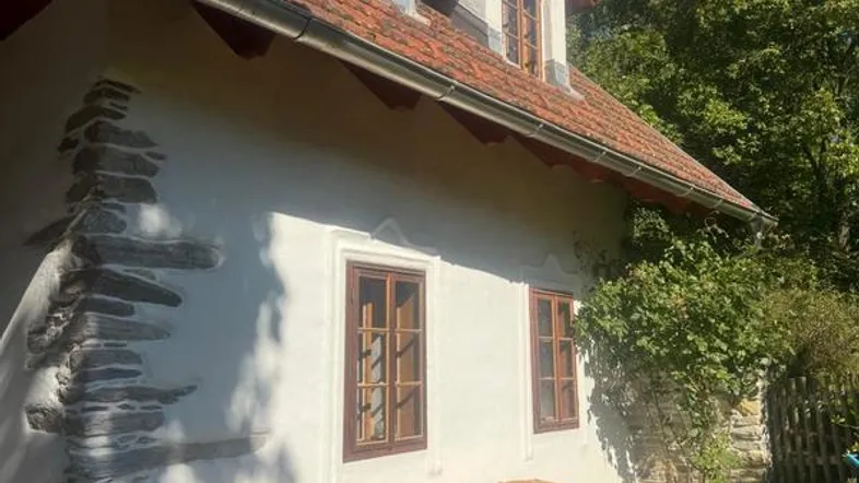 Traditionelles Landhaus mit weißer Fassade, roten Dachziegeln und gestapeltem Brennholz im Vorgarten.