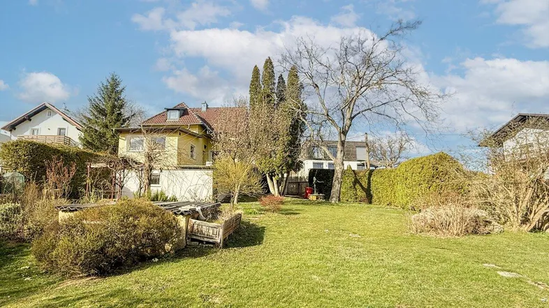 Großzügiger Gartenbereich mit Rasenfläche und Blick auf das Wohnhaus unter blauem Himmel.