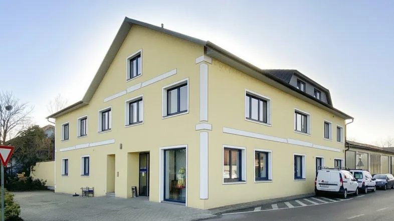 Gelbes Geschäftsgebäude mit moderner Architektur, vielen Fenstern und Parkplätzen an der Straße.