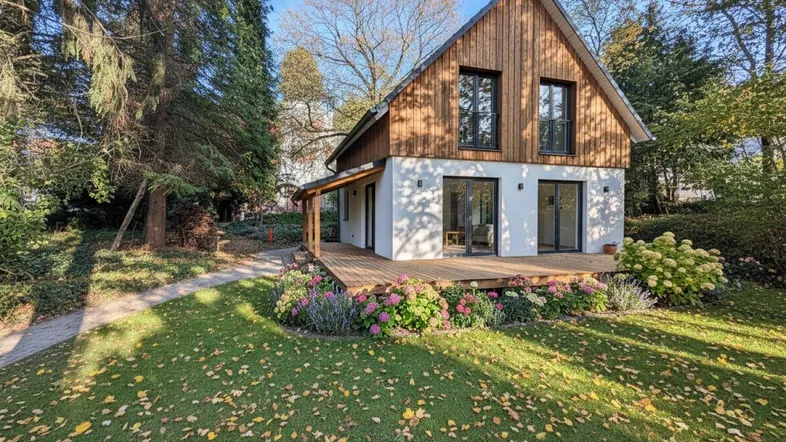 Modernes Einfamilienhaus mit Holzfassade, großer Holzterrasse und gepflegtem Garten mit bunten Blumenbeeten.