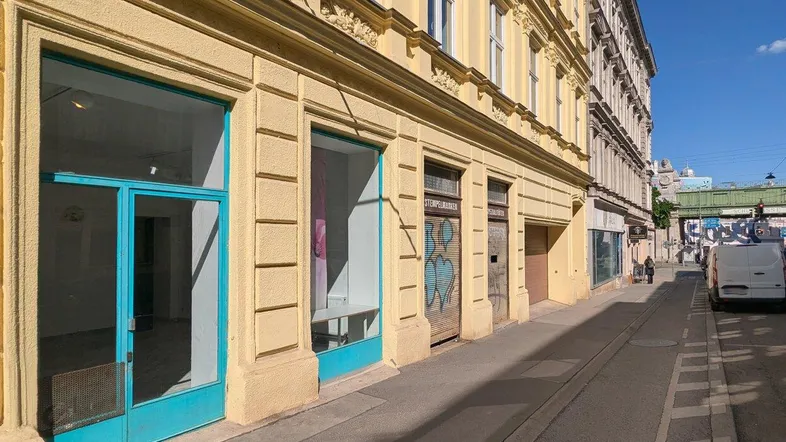 Gelbe Fassade eines Altbaus mit mehreren Ladenlokalen und türkisfarbenen Türen im Erdgeschoss.