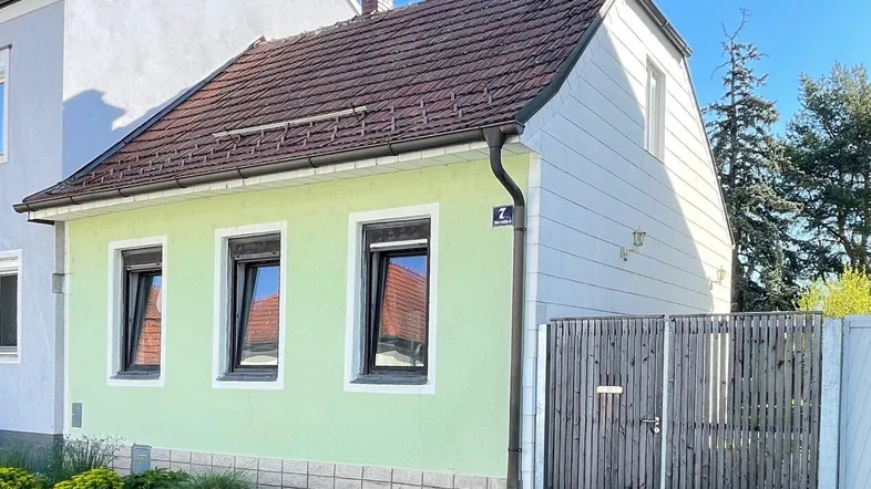 Kleines Einfamilienhaus mit hellgrüner Fassade, Satteldach und Holzzaun.