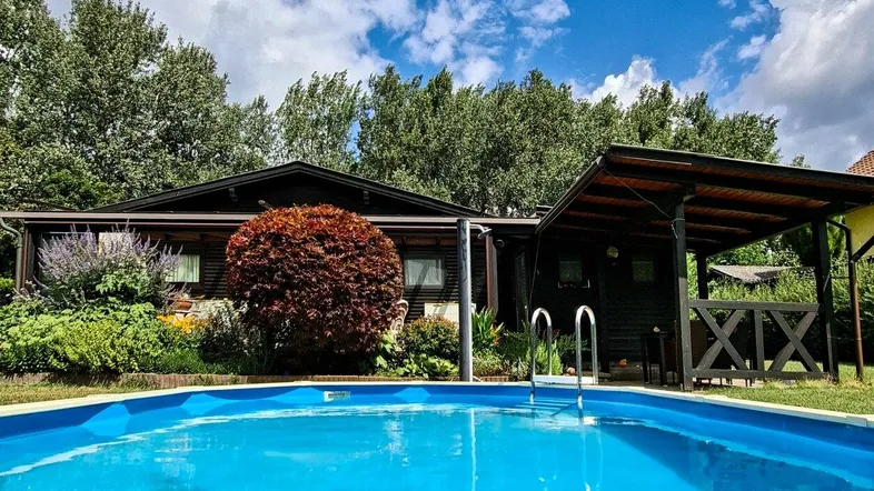 Holzhaus mit erfrischendem Pool und überdachtem Sitzbereich im grünen Garten.