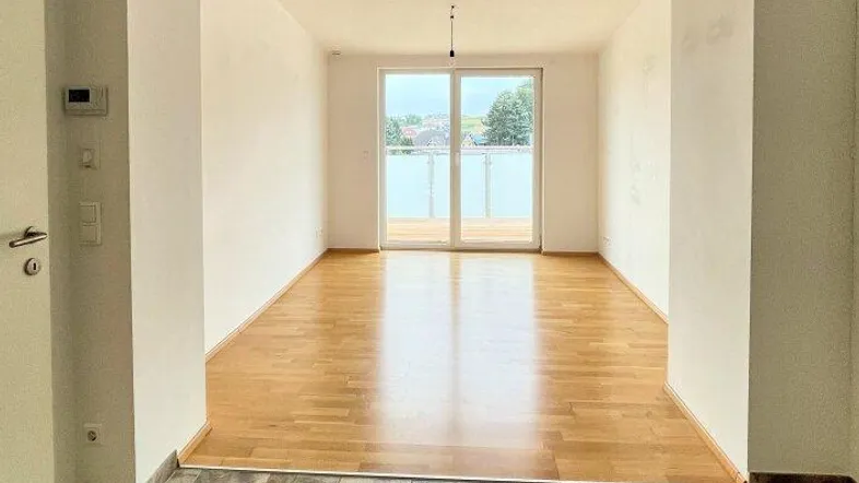 Helles, leeres Wohnzimmer mit Holzboden und Zugang zu einem Balkon, bereit zur Einrichtung.