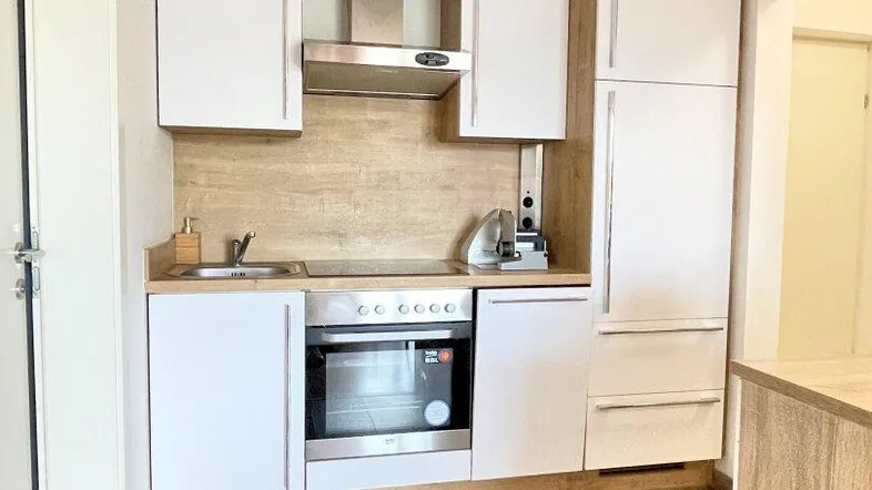 Moderne Einbauküche mit weißen Fronten, Holzdetails, integrierten Geräten und Fliesenboden.