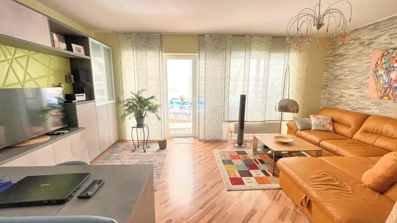 Helles Wohnzimmer mit bequemer Ledercouch, Holzboden und Zugang zu einem sonnigen Balkon.
