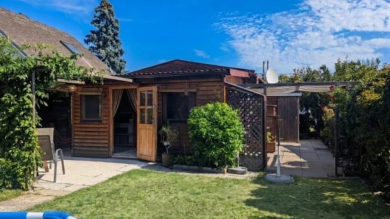 Gemütlicher Gartenbereich mit Holzhaus, Terrasse und einem aufstellbaren Pool unter blauem Himmel.