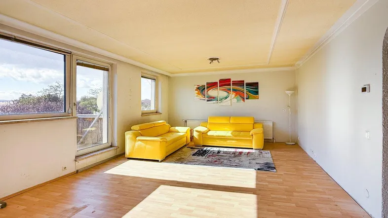 Helles Wohnzimmer mit Parkettboden, gelben Sofas und Zugang zu einem Balkon.