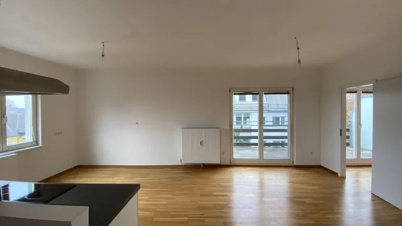 Geräumiger offener Wohnbereich mit Parkettboden, großen Fenstern und Zugang zu einem Balkon.