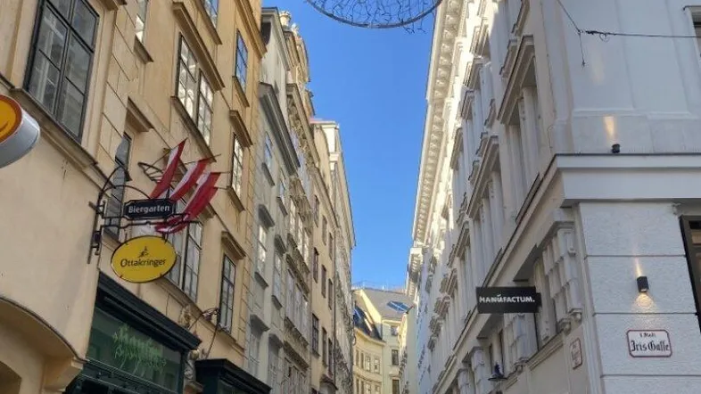 Enge Gasse in einer historischen Stadt mit Geschäften und Gebäuden unter blauem Himmel.