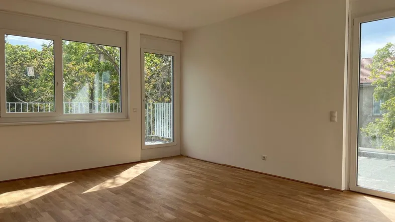 Helles Zimmer mit Holzboden und Zugang zu einem Balkon oder einer Terrasse, ideal für Wohnzwecke.