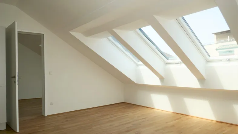 Helles Dachgeschosszimmer mit schrägen Wänden, Holzboden und mehreren Dachfenstern für viel Tageslicht.