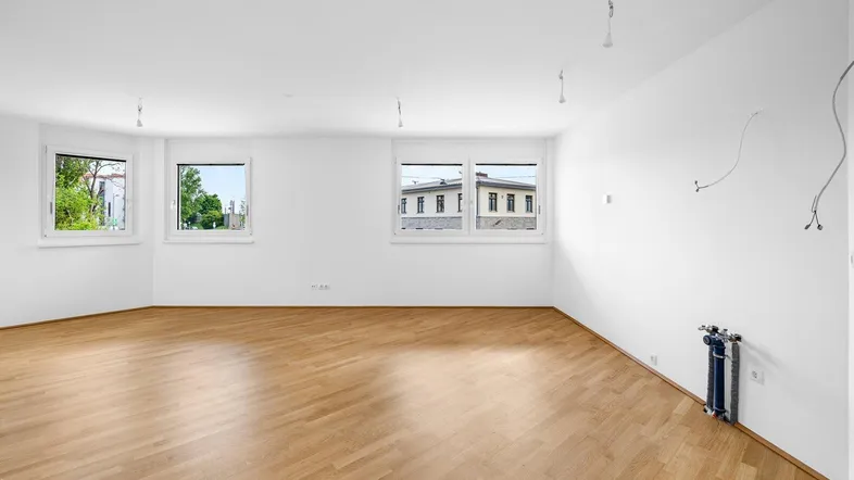 Helles, leeres Zimmer mit Parkettboden und mehreren Fenstern, bereit zur individuellen Gestaltung.