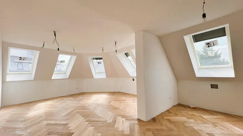 Heller Dachgeschossraum mit Fischgrätparkett und mehreren Dachfenstern, bereit für den Ausbau.
