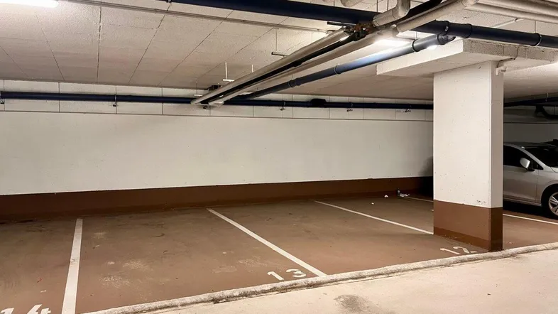 Tiefgarage mit markierten Stellplätzen und sichtbaren Versorgungsleitungen an der Decke.