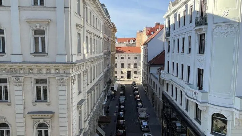 Blick von oben auf eine belebte Stadtstraße mit historischen Gebäuden und blauem Himmel.