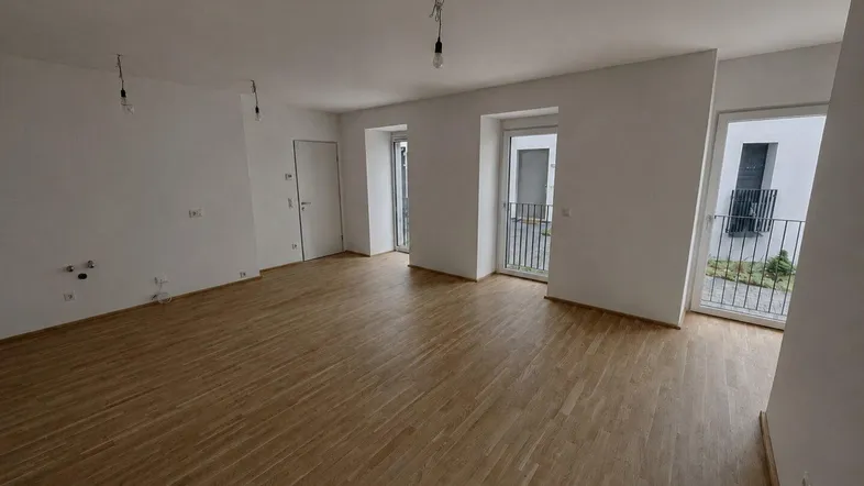Heller, leerer Wohnraum mit Parkettboden und Zugang zu französischen Balkonen in einem Neubau.