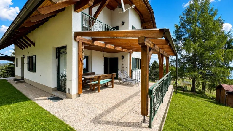 Geräumige Terrasse mit Holzpergola und Sitzgelegenheiten, umgeben von grüner Landschaft und Bergblick.