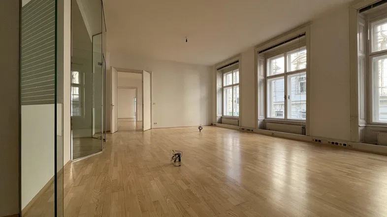 Geräumiger, heller Raum mit Holzboden, großen Fenstern und einer modernen Glaswand.