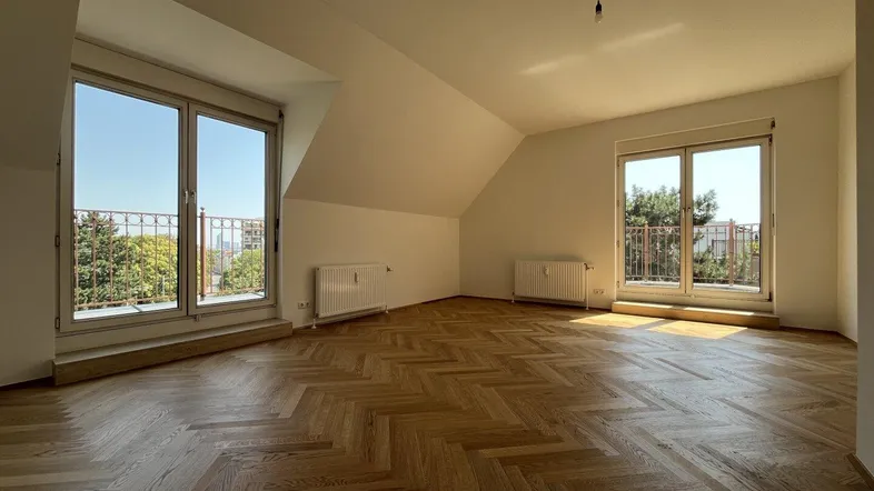 Helles Zimmer mit Fischgrätparkett, Dachschrägen und Zugang zu zwei französischen Balkonen.