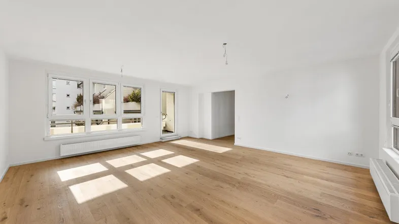 Geräumiges, helles Wohnzimmer mit Holzboden und viel Tageslicht durch die Fenster.