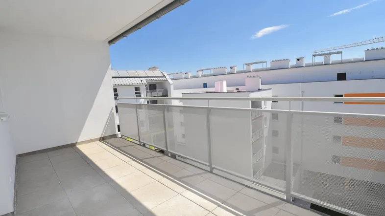 Heller Balkon mit Fliesenboden und Blick auf die umliegenden Gebäude unter blauem Himmel.