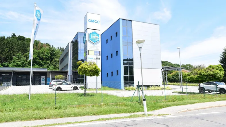 Modernes Bürogebäude mit blauer Glasfassade und umliegenden Parkplätzen unter blauem Himmel.