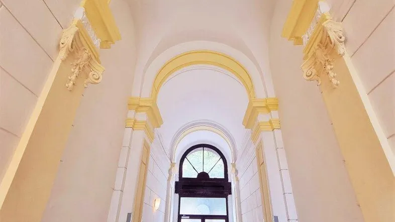 Historischer Eingangsbereich mit hohen Gewölbedecken und dekorativen Stuckelementen, der zum Gebäude führt.