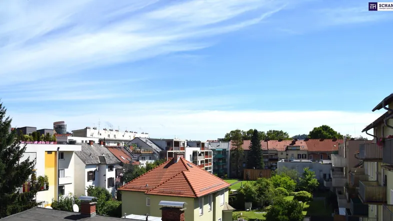 Blick über die Dächer einer Wohnsiedlung mit blauem Himmel und vereinzelten Wolken.