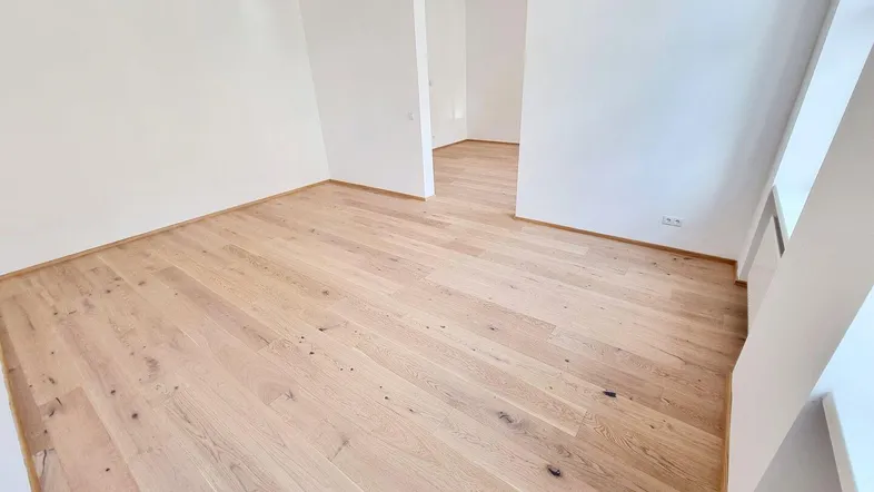 Helles Zimmer mit neuem Parkettboden und weißen Wänden, bereit zur individuellen Gestaltung.