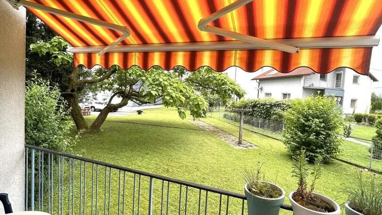 Geräumiger Balkon mit gestreifter Markise, Gartenmöbeln und Blick ins Grüne.