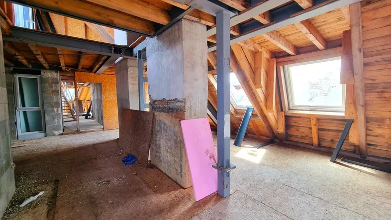 Unfertiger Dachbodenraum mit sichtbaren Holzbalken und Metallstützen, bereit für den Ausbau.