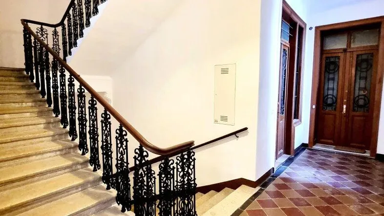 Elegantes Treppenhaus eines Altbaus mit schmiedeeisernem Geländer und Terrakotta-Fliesenboden.