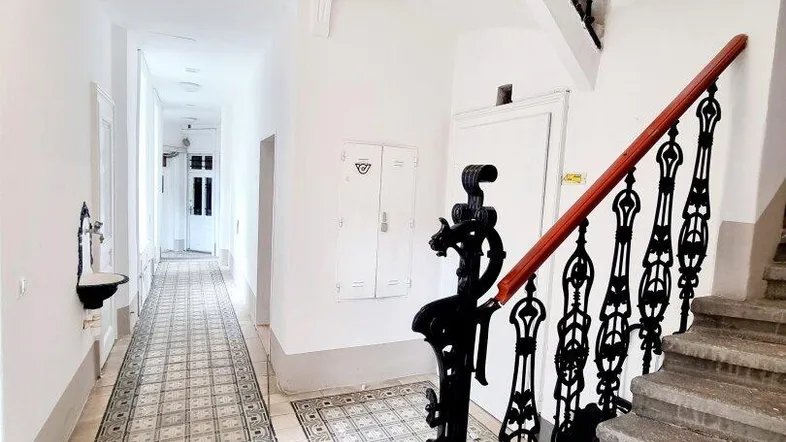 Helle Eingangshalle mit historischem Fliesenboden und schmiedeeisernem Treppengeländer in einem Altbau.