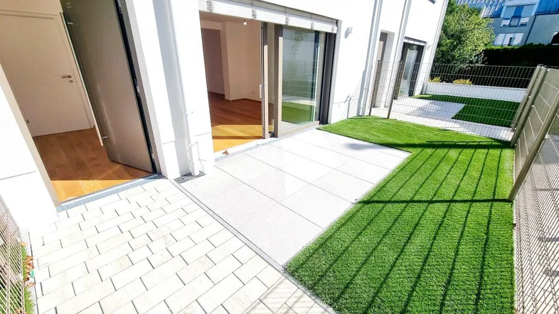 Helle Terrasse mit Kunstrasenfläche und Zugang zu den Innenräumen eines modernen Gebäudes.