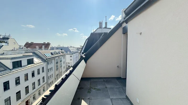 Geräumige Dachterrasse mit Fliesenboden und weitem Blick über die Dächer der Stadt unter strahlendem Sonnenschein.