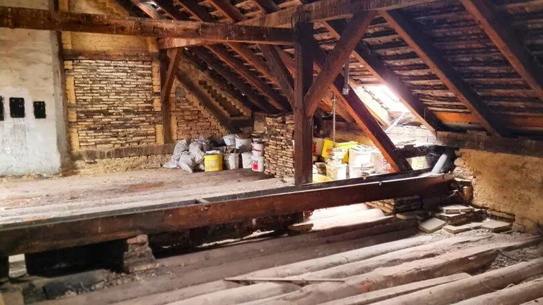 Geräumiger Rohdachboden mit sichtbaren Holzbalken und Ziegelwänden, bietet Potenzial für Ausbau.
