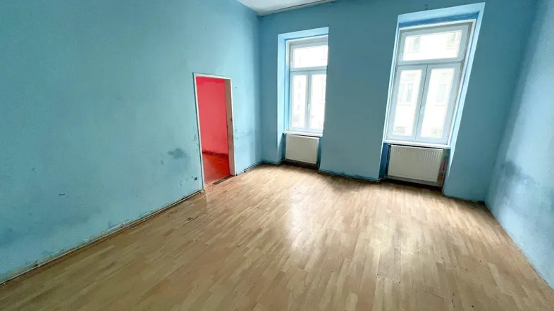 Geräumiger Raum mit hellblauen Wänden, Holzfußboden und zwei Fenstern, bereit zur Renovierung.